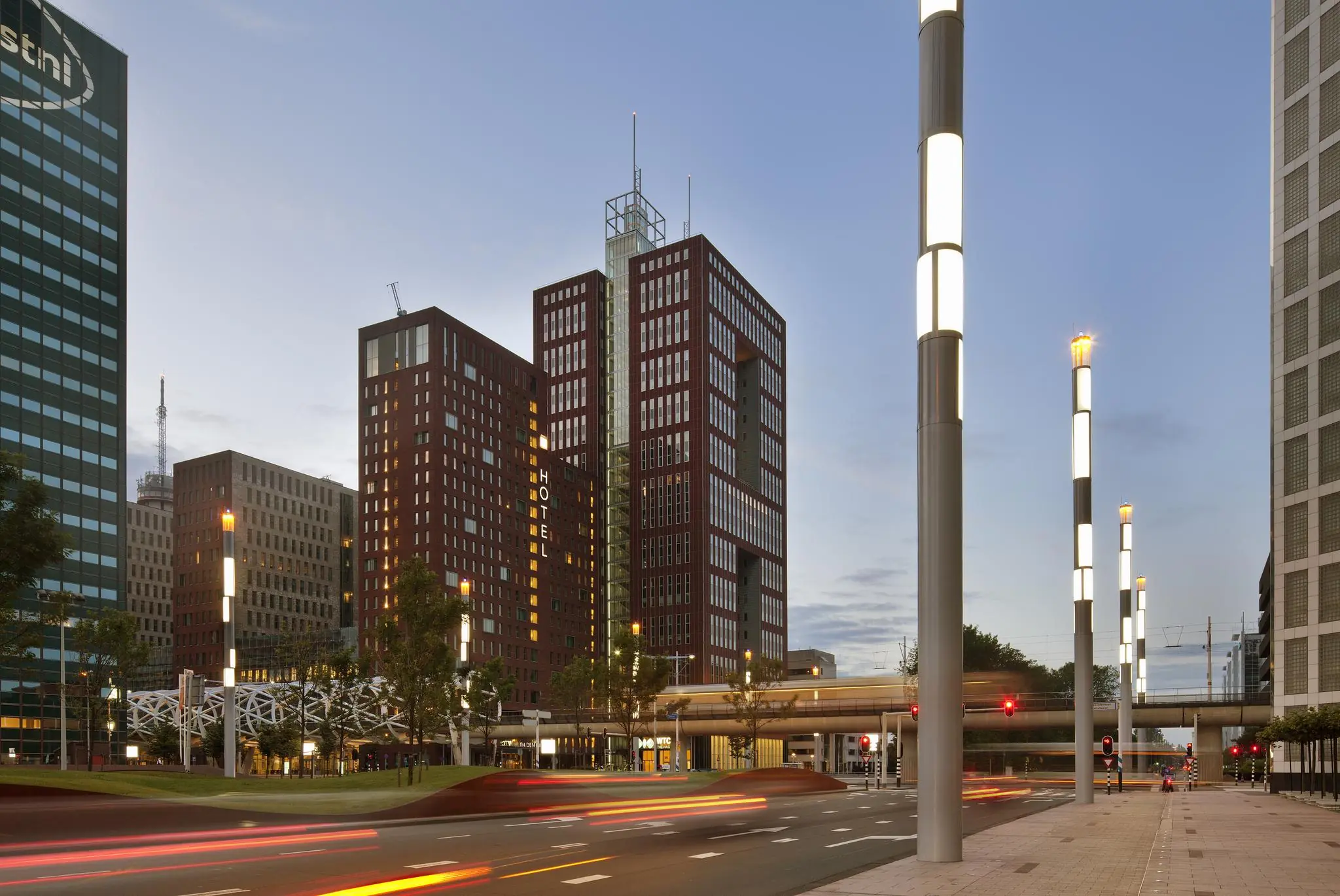 Straatbeeld van de Prinses Beatrixlaan in Den Haag met moderne hoogbouw, lichtmasten en voorbijrijdend verkeer in de schemering.